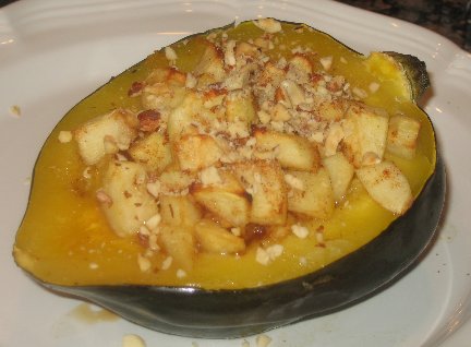 Half of an acorn squash, baked with stuffed with an apple filling on a white plate.