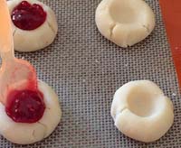 Unbaked thumbprint cookie dough being filled with jam.