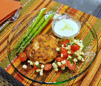 Crab Cakes with Tomato Corn Salad on a clear glass plate on a colorful striped placemat