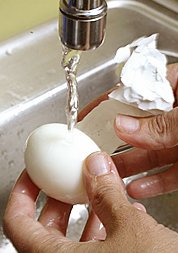 two hands holding a hard boiled egg under a running tap