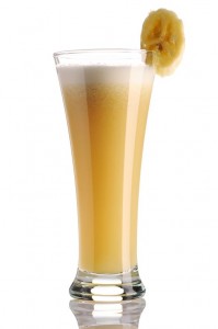 Smoothie in a tall glass with banana slice on glass rim