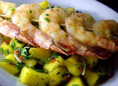 Mango Salad with Grilled Shrimp on a skewer laid across on a white plate