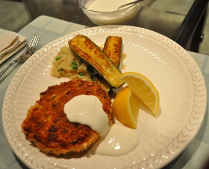 salmon Cakes with sauce and cucumber garnished with lemon slices on a white plate