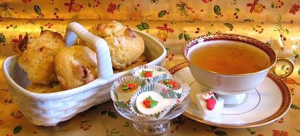 basket of honey butterscotch-ginger tea scones and a teacup on a saucer next to a glass bowl with tea mini cakes