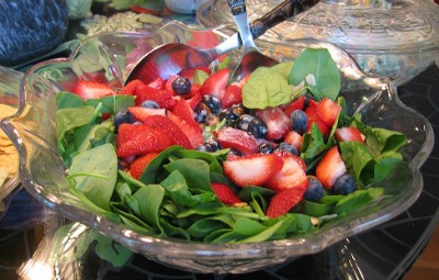 Spinach Salad with Strawberries in a large glass bowl with metal serving spoons