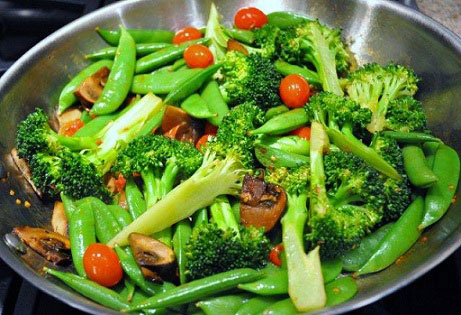 Stir Fry snow peas with broccoli and mushrooms in a frying pan.