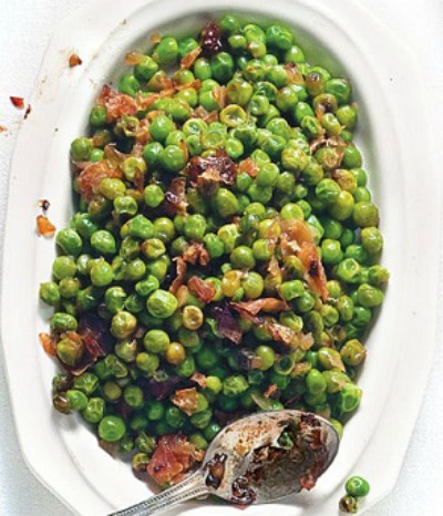 Sweet Peas with Prosciutto in a large white serving dish with a spoon