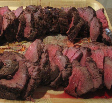 Peppery Pinot Noir Tenderloin Roast sliced up and arranged on a wooden cutting board