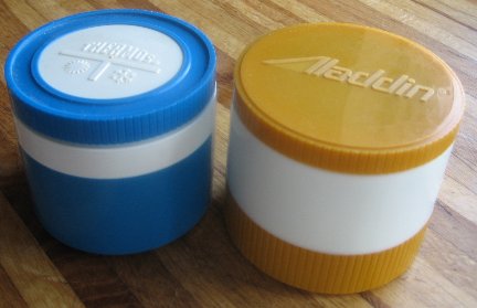 two small thermoses used for storing condiments sitting on a wooden table