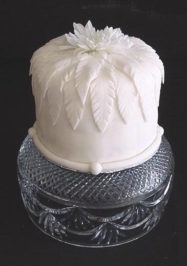 tall round cake decorated with a flower made of white fondant sitting on a cake stand