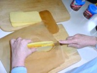 Two hands slicing the cake in half over the wax paper lined cutting board