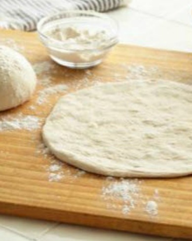 pizza dough being prepared on wooden cutting board