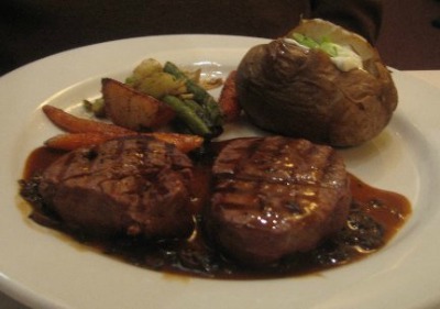 grilled beef tenderloin on a white plate with baked potato and carrots