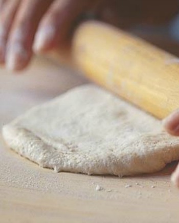 thin crust pizza dough being rolled our on floured wooden block