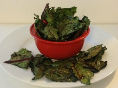 Red bowl of Baked Beet Green Chips surround by Baked beet greens on plate