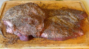 raw beef brisket covered in seasoning on a wooden cutting board