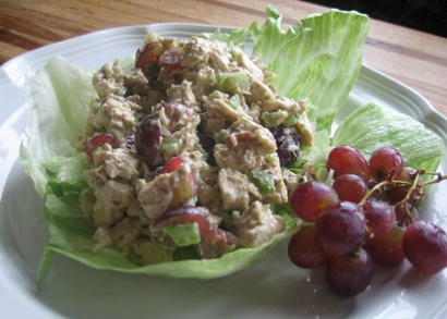 Chicken Salad on cabbage leaf with red grapes on the side served together on a white plate