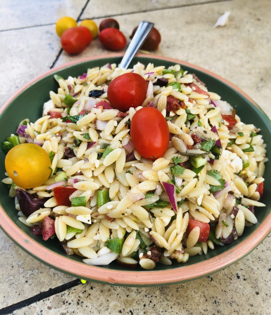 Greek Orzo Salad in a green bowl with cherry tomatoes 