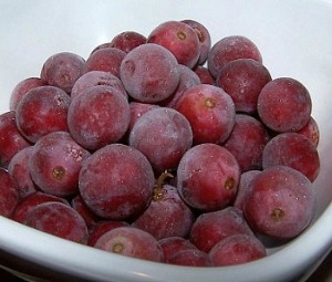 A pile of frozen red grapes in a white bowl