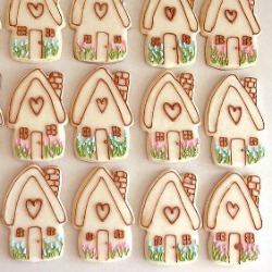 many completed Ginger Bread House Cookies in rows on a white surface