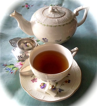 afternoon tea in a delicate white cup and saucer next to a white tea kettle on a baby blue napkin