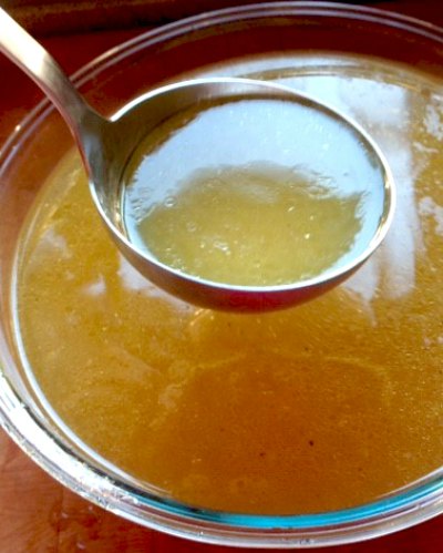 chicken stock being ladled out of a glass bowl